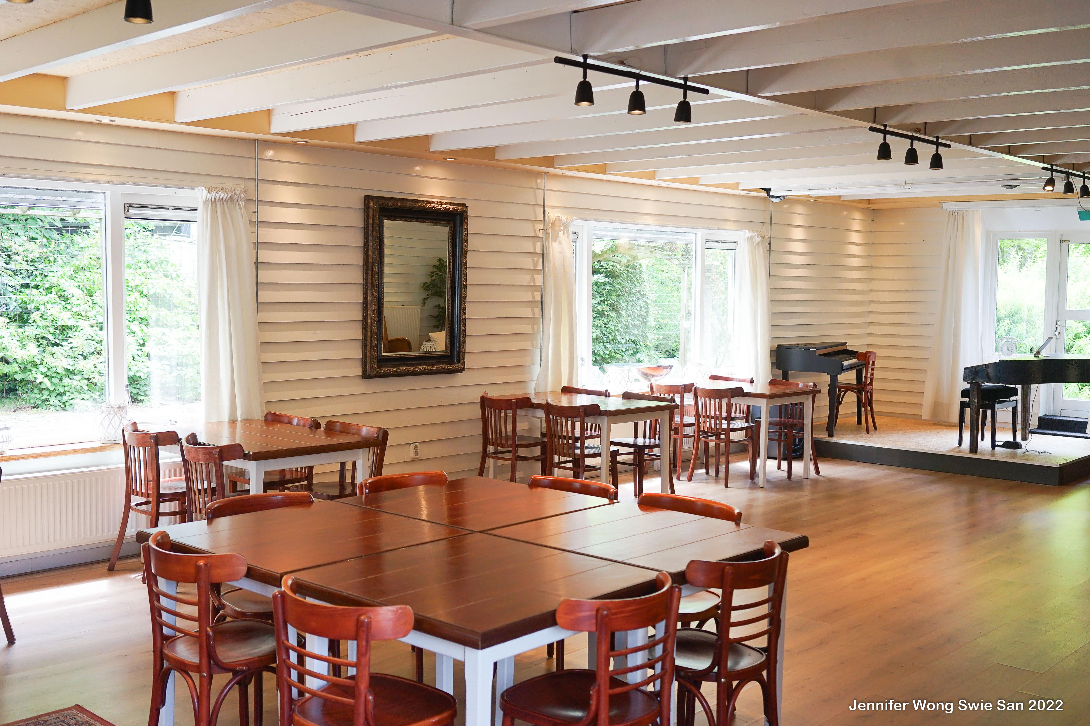 Kleine tuinzaal van Wit Kerkje met vleugelpiano, houten tafels en grote ramen