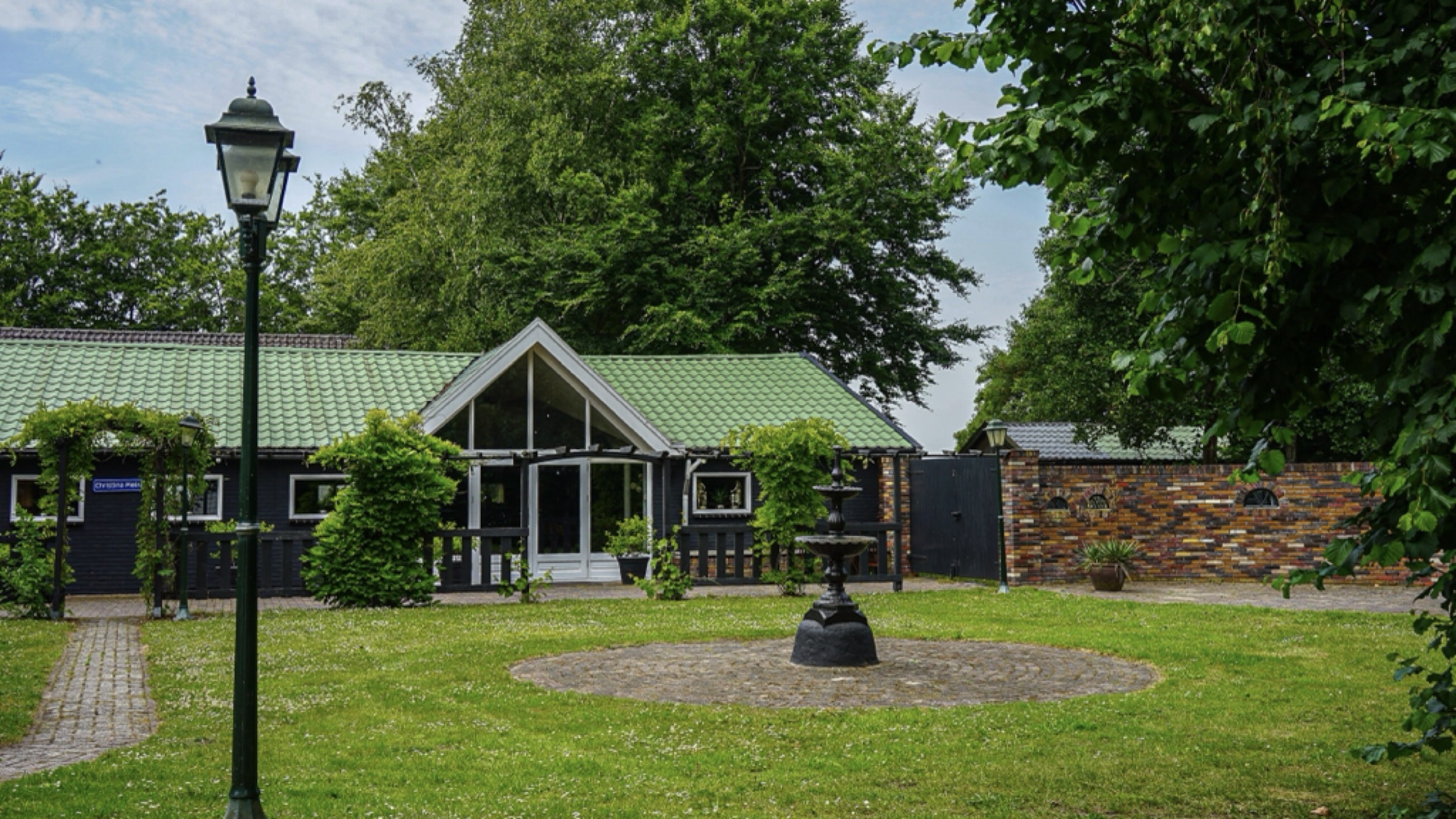 Binnenplein van Wit Kerkje met sierfontein, lantaarnpaal en groene dakkapel omgeven door bomen